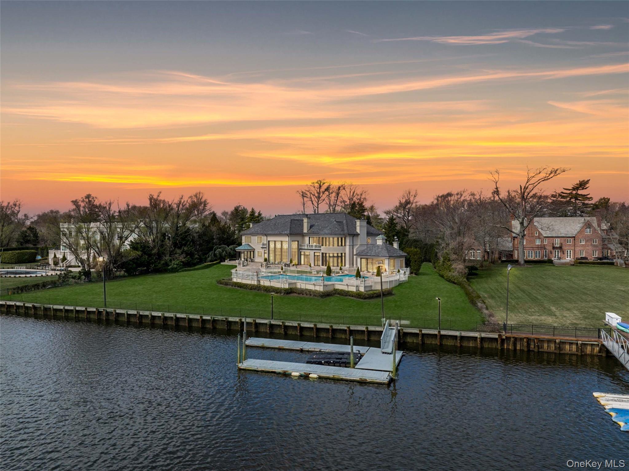 Waterfront home with a pool and private dock, viewed across the water at sunset.