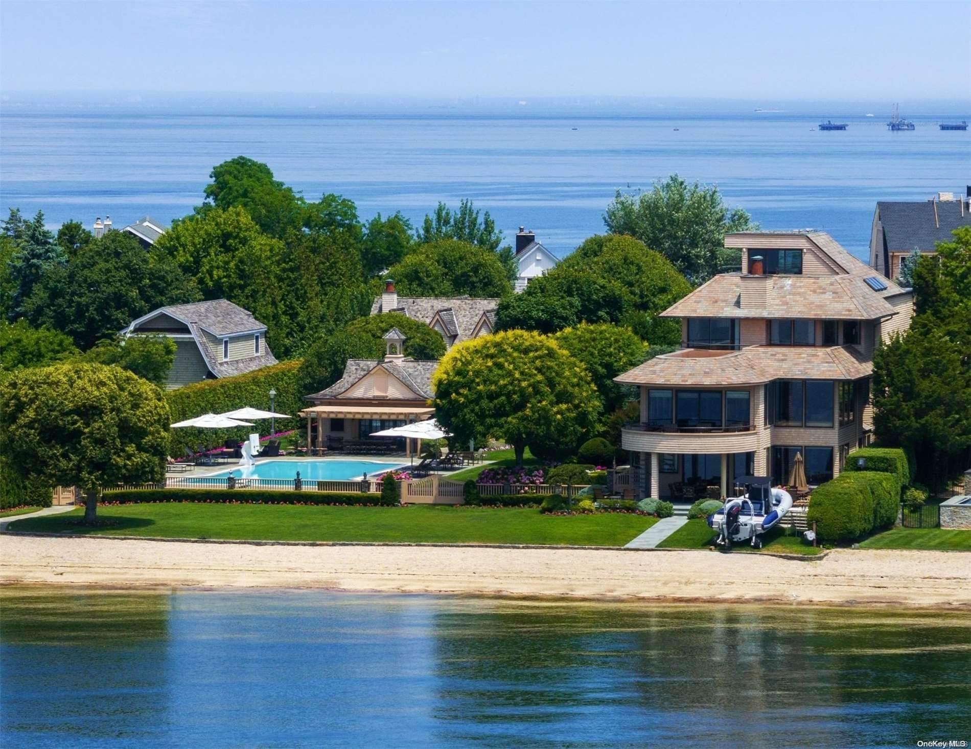 Shingle-style waterfront home with a pool, landscaped grounds, and sandy shoreline.