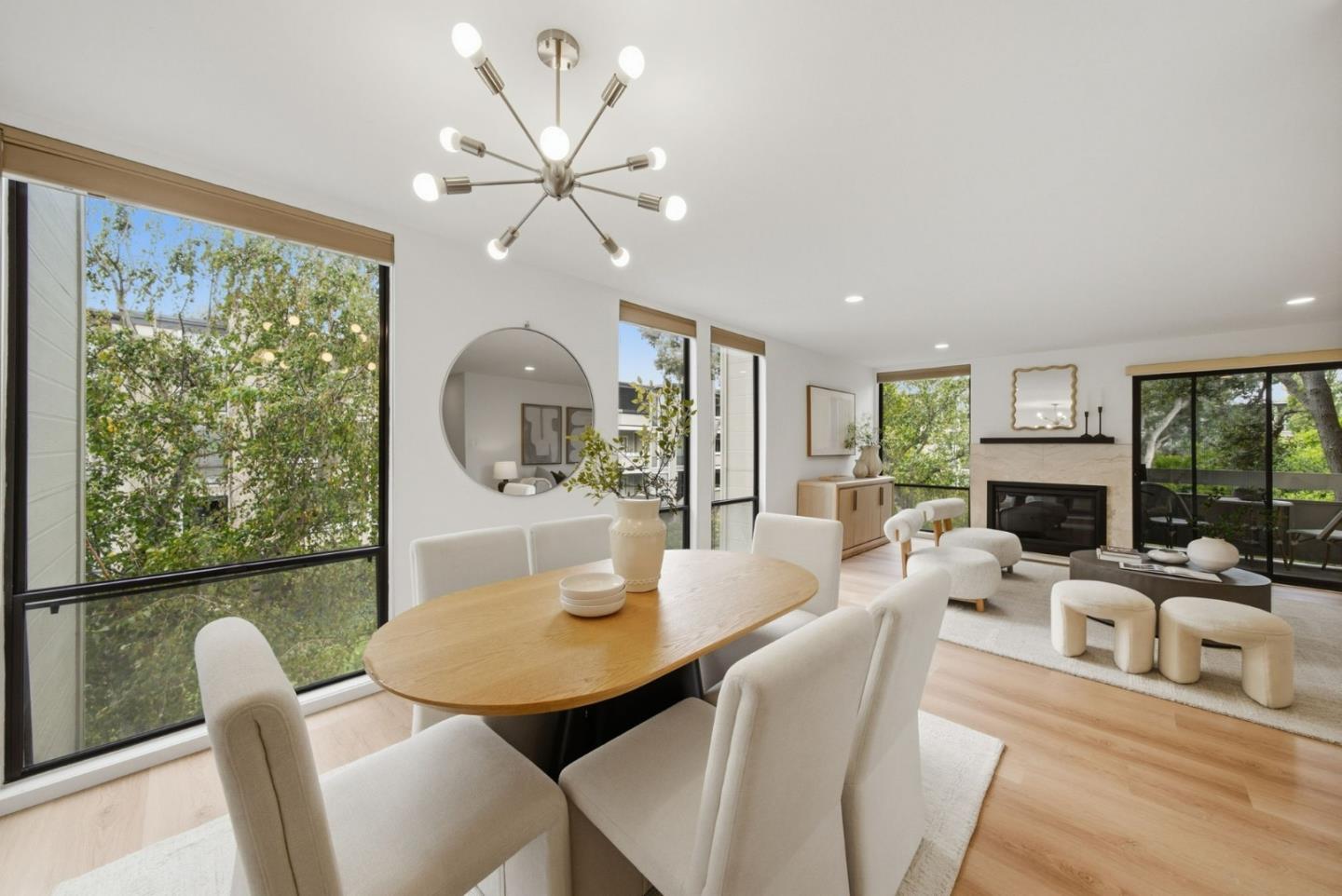 Open-plan dining and living room with large windows, a marble-surround fireplace, and light wood floors.