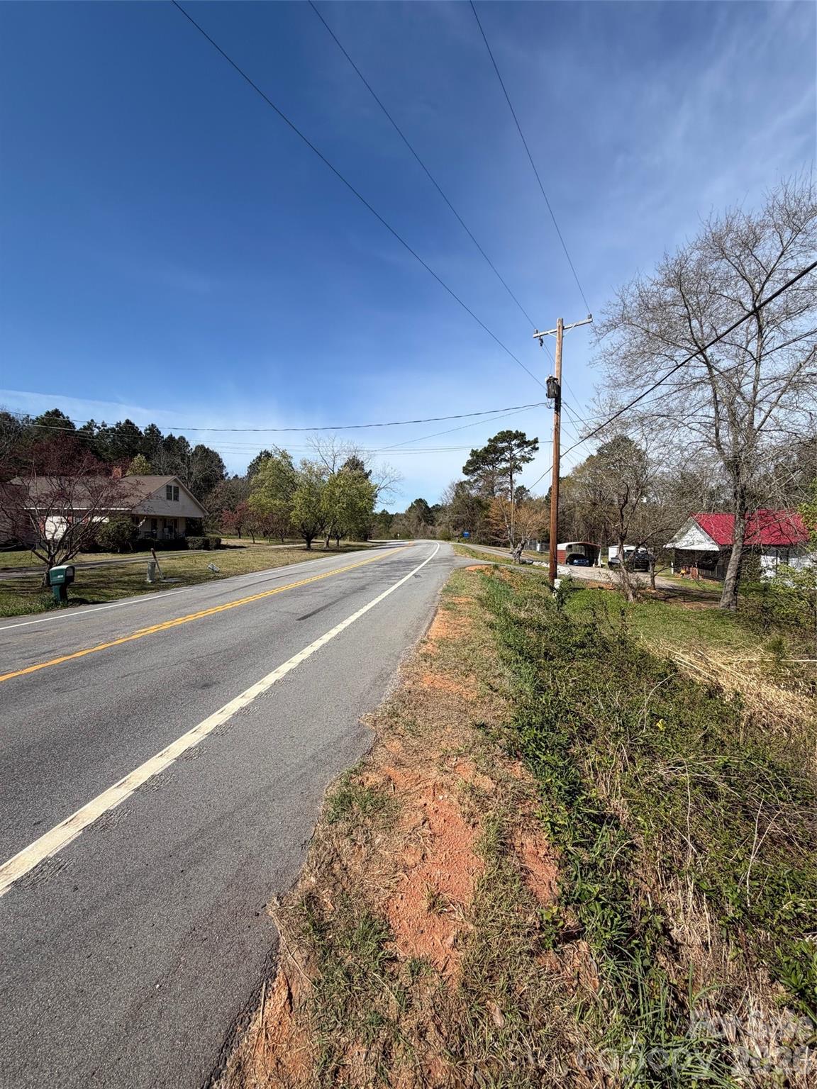 Two-lane highway curves past grassy roadside, utility poles, and nearby homes.