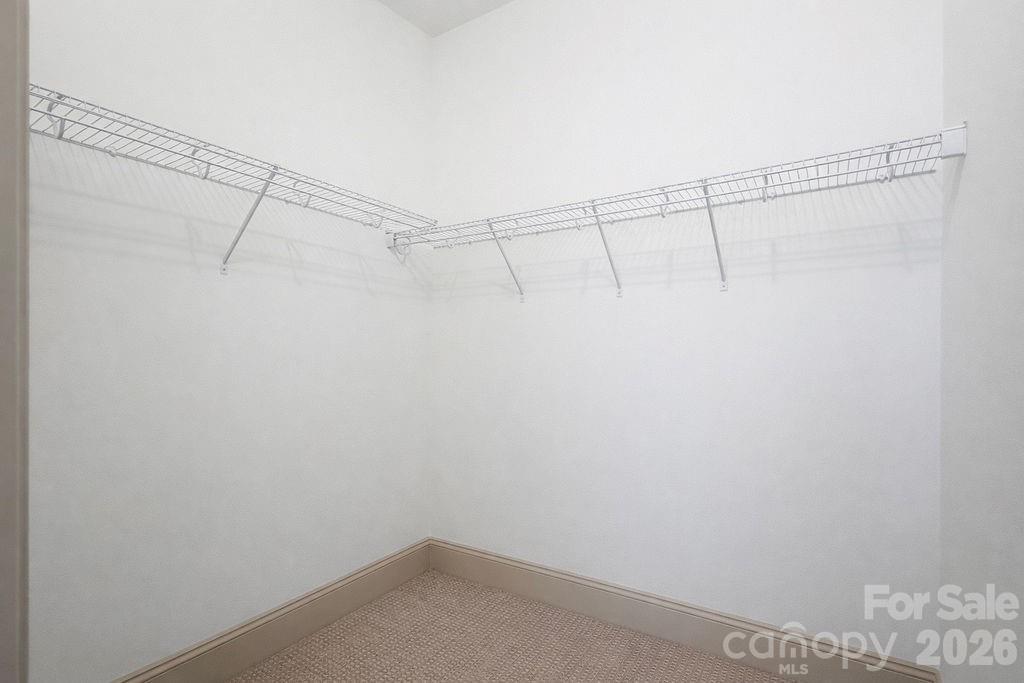Empty walk-in closet with wire shelving around two walls and beige carpet.