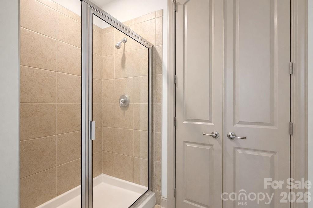 Bathroom shower with beige tile, glass enclosure, chrome fixtures, and white double doors.