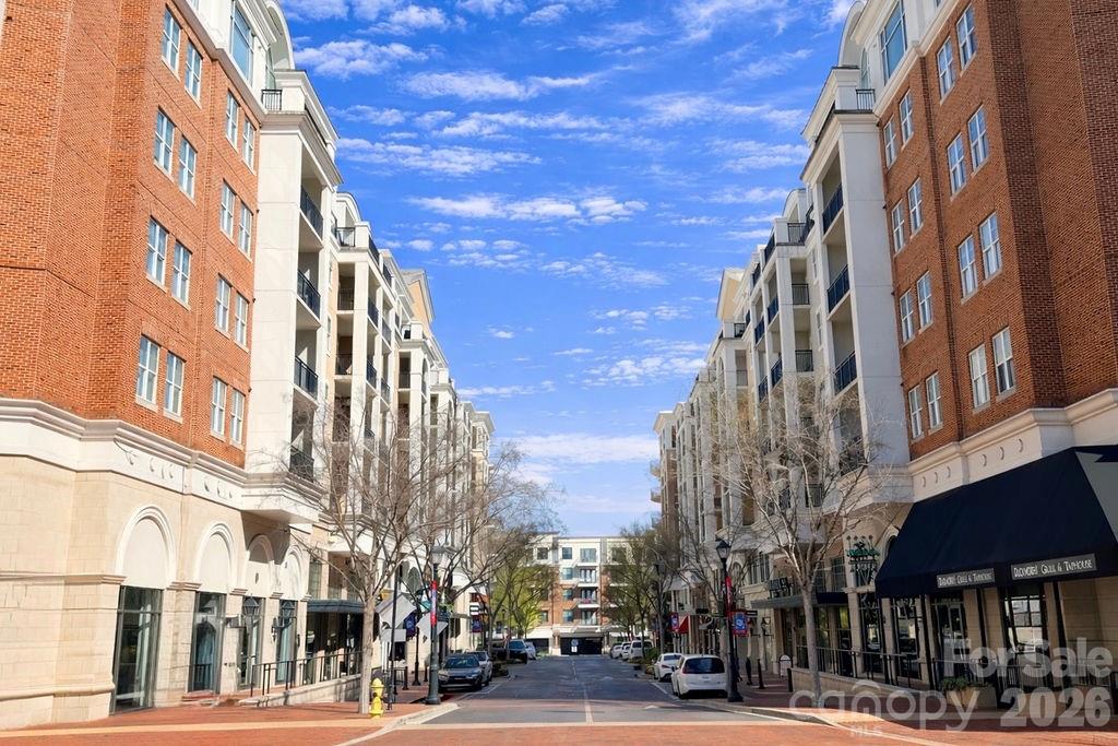 Piedmont Row streetscape between brick-and-stone buildings, with storefronts and parked cars beneath a blue sky.