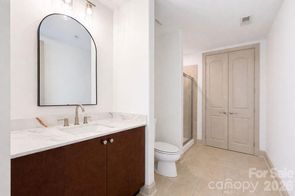 Bathroom with a dark wood vanity, marble-look counter, arched mirror, toilet, and glass shower.