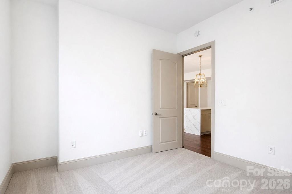 Empty carpeted room with an open doorway to a bathroom vanity.