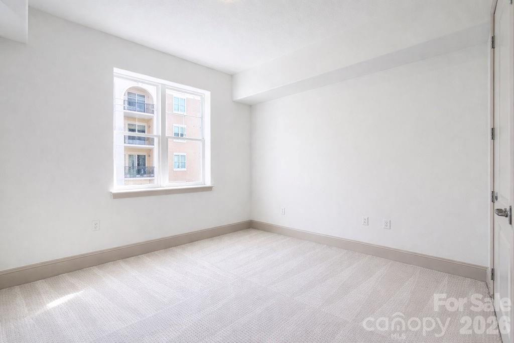 Vacant carpeted bedroom with a large window overlooking a neighboring apartment building.