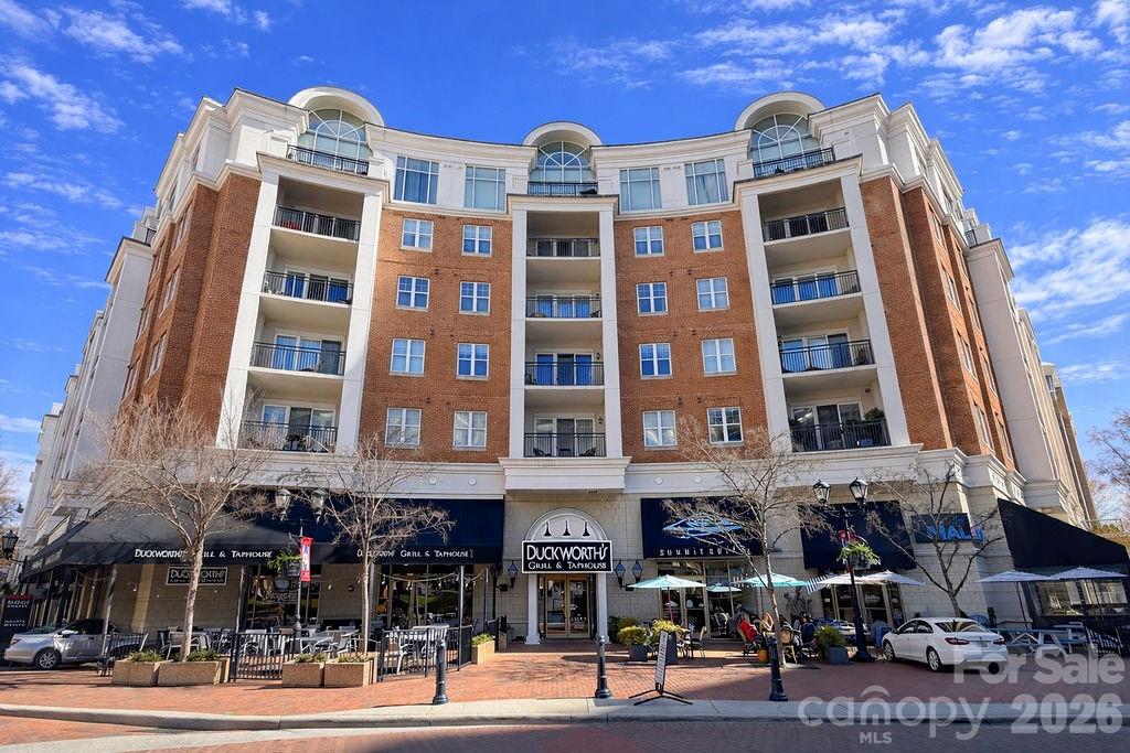 Brick condominium building with rows of balconies above ground-floor shops and restaurants.