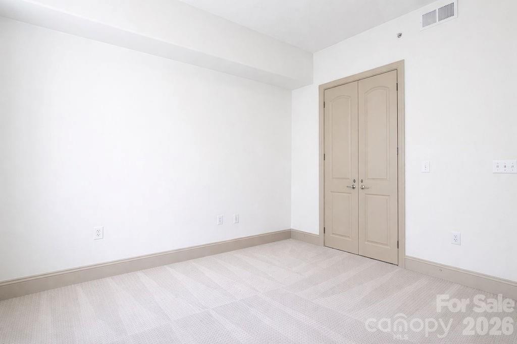 Empty carpeted room with closed double closet doors and white walls.