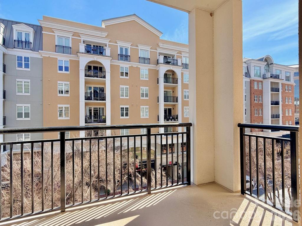Apartment balcony with black railings overlooking multistory buildings and storefronts.