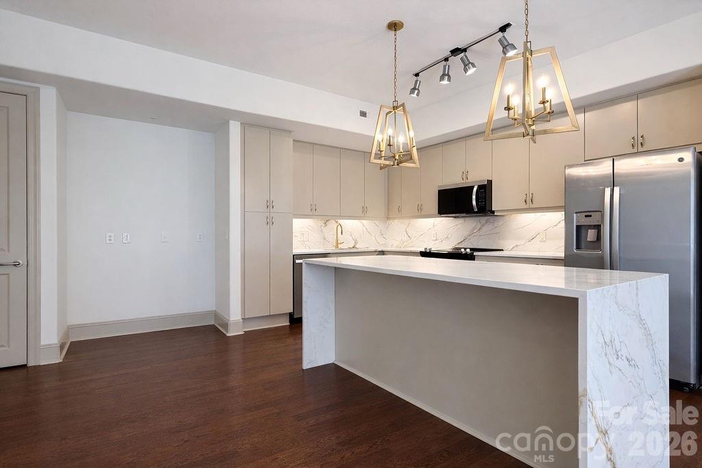 Modern vacant kitchen with a large marble island, stainless steel appliances, and pendant lights.