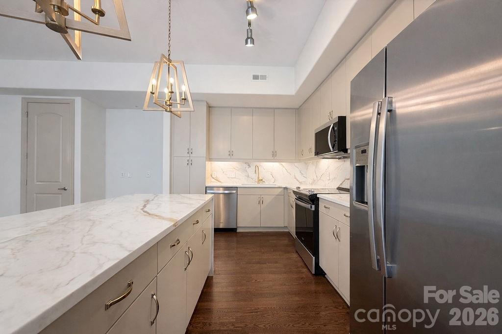Modern kitchen with a long marble-look island, white cabinetry, and stainless-steel appliances.