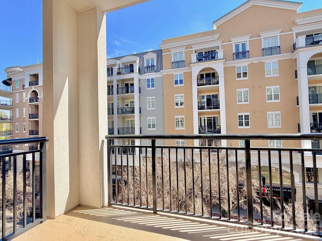 Apartment balcony overlooking a peach-and-gray building, with black railings and bare trees below.