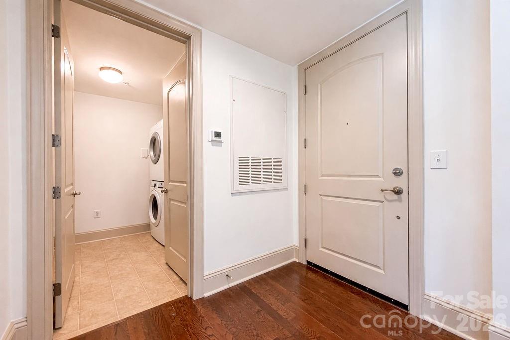 Entry hall with front door and open laundry closet containing stacked washer and dryer.