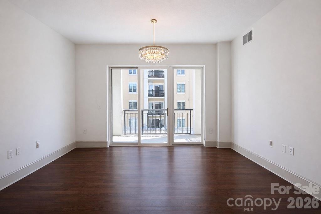 Vacant room with dark hardwood floors, a crystal chandelier, and sliding doors to a balcony.
