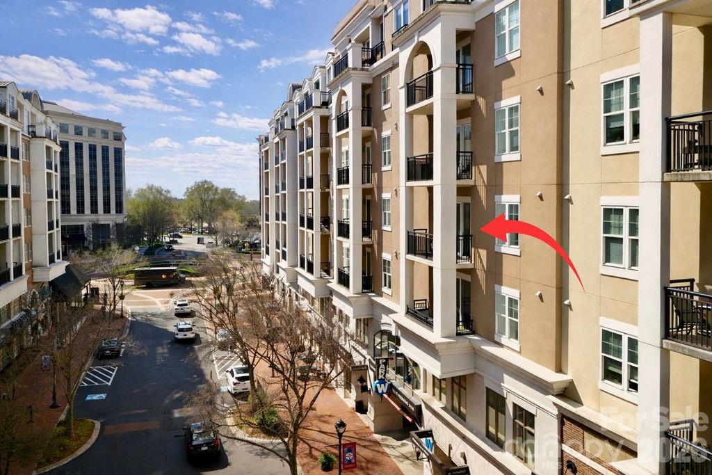 Tan multi-story building with balconies, marked by a red arrow pointing to a window.