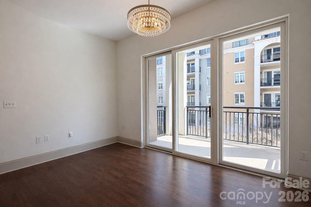 Empty room with dark hardwood floors, a crystal chandelier, and sliding glass doors to a balcony.