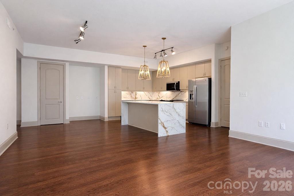 Open-plan kitchen with marble-look island, beige cabinets, stainless steel appliances, and dark hardwood floors.