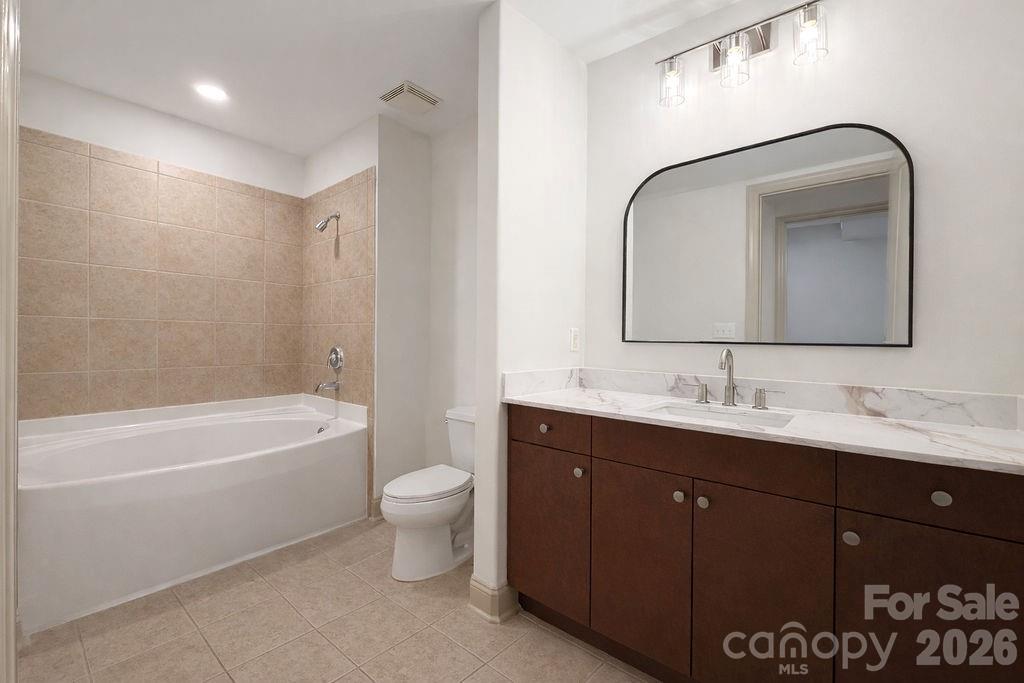 Bathroom with a tiled bathtub surround and dark wood vanity beneath a large arched mirror.