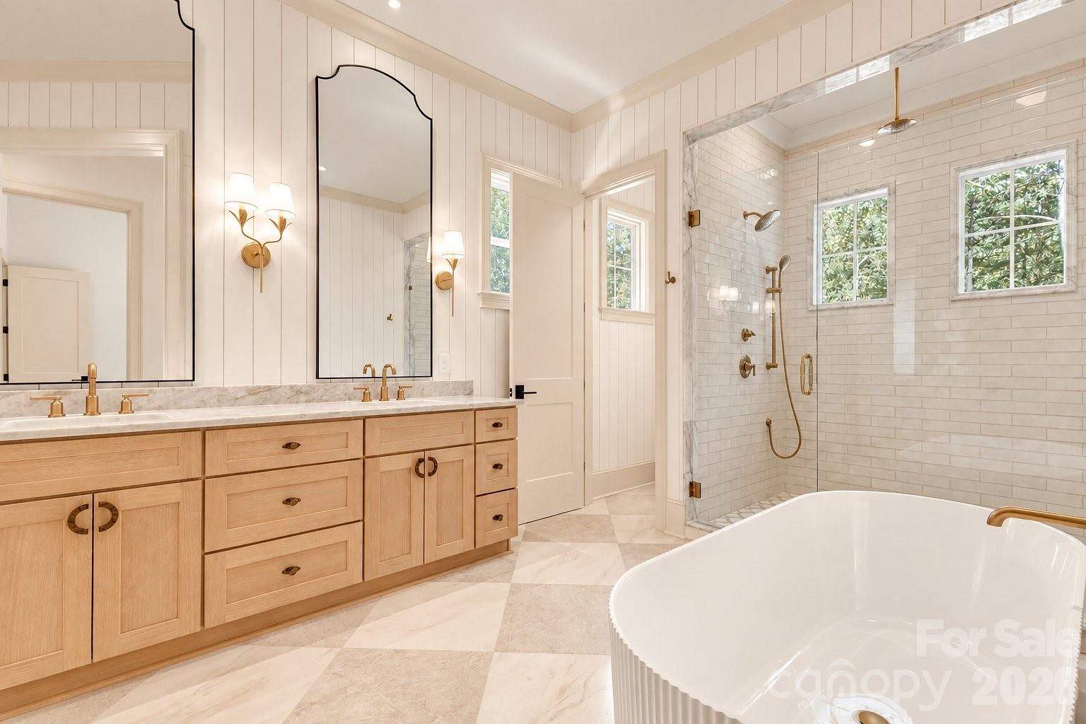 Bathroom with a light wood double vanity, freestanding tub, and glass shower with brass fixtures.