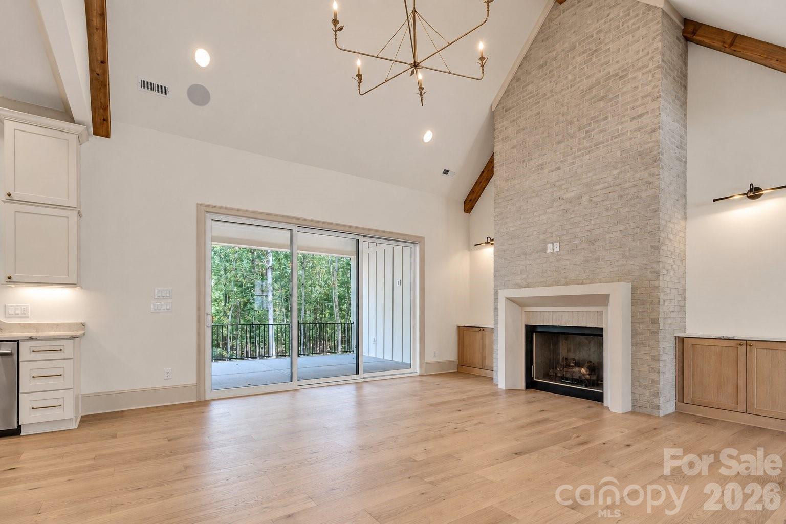 Living room with vaulted ceiling, brick fireplace, and sliding doors opening to a wooded balcony.