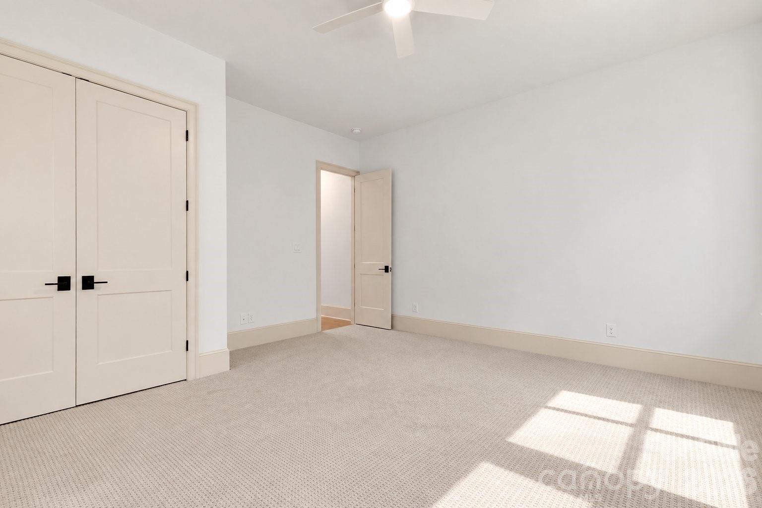 Empty bedroom with beige carpet, double closet doors, and sunlight across the floor.