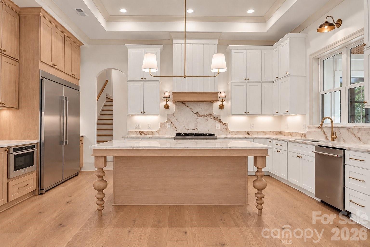 Renovated kitchen with a large wood island, white cabinetry, marble surfaces, and stainless steel appliances.
