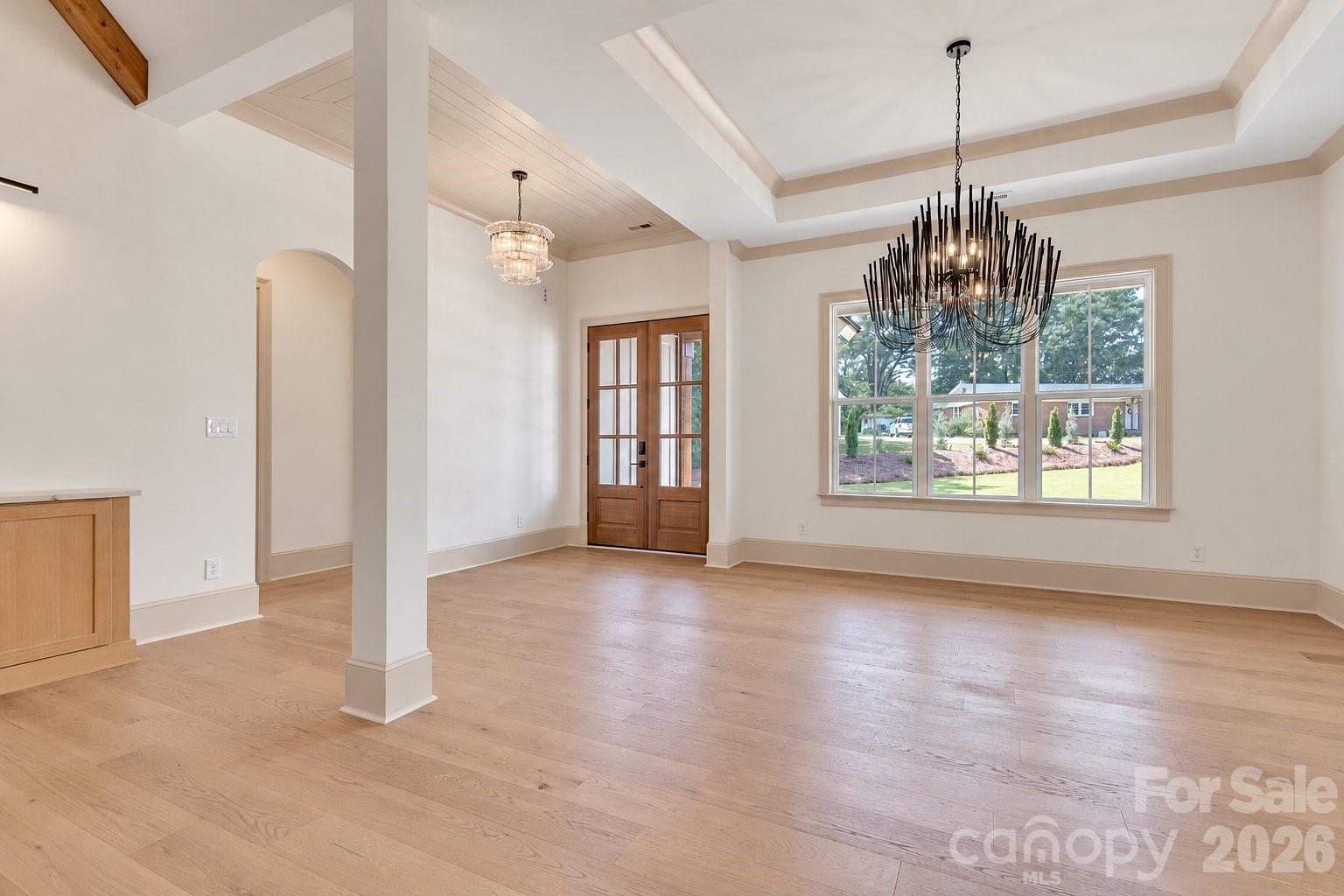 Vacant dining room with a tray ceiling, statement chandelier, hardwood floors, and wood-framed glass doors.