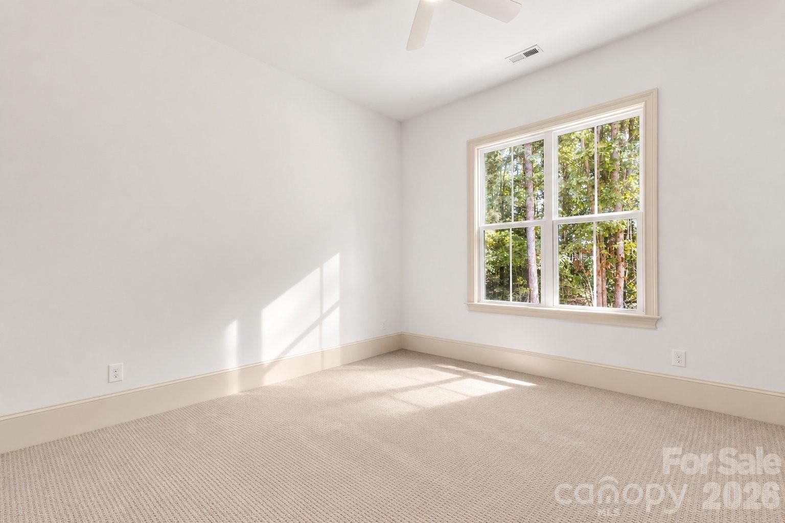 Vacant carpeted bedroom with a large window overlooking trees and sunlight on the walls.