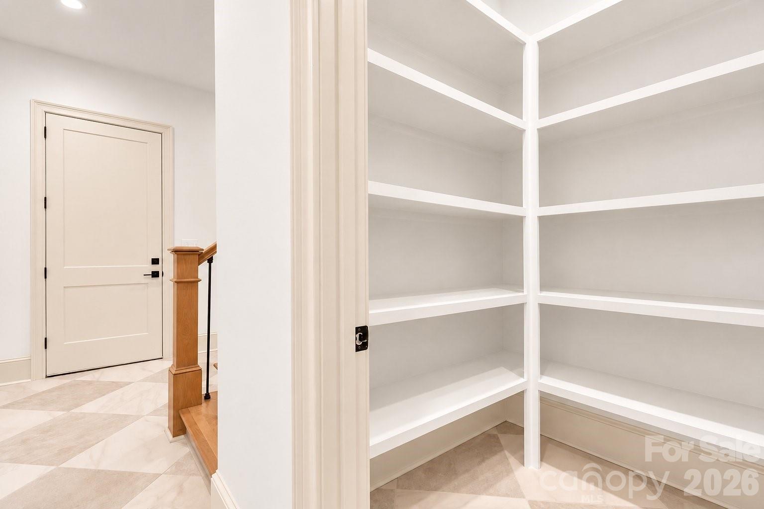 Entryway with empty built-in corner shelves beside a paneled door and wooden stair railing.