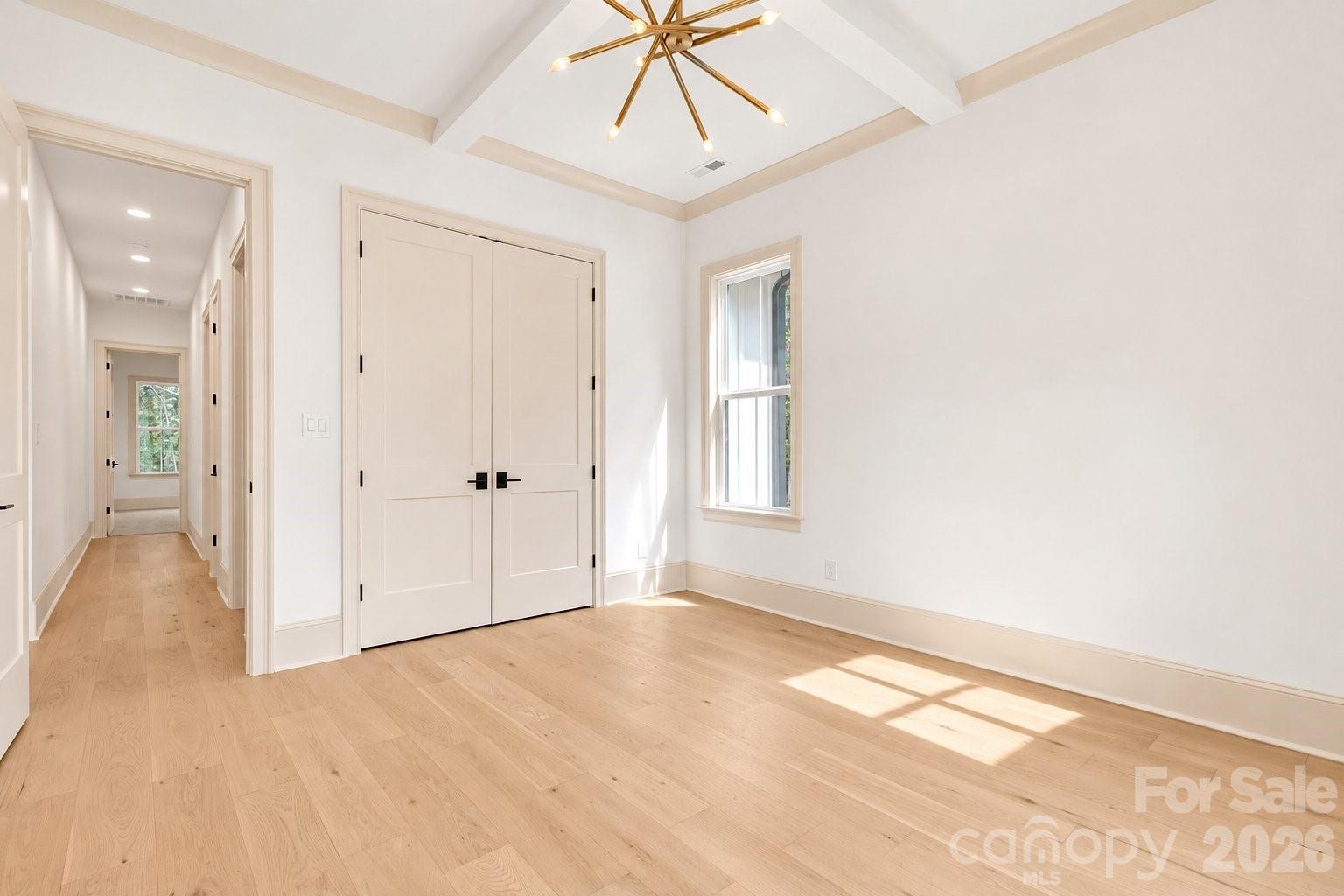 Vacant room with pale wood floors, vaulted beamed ceiling, double closet doors, and a hallway entrance.