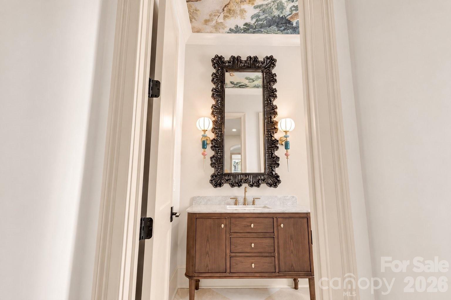 Powder room with a walnut vanity, marble counter, ornate mirror, and globe sconces.