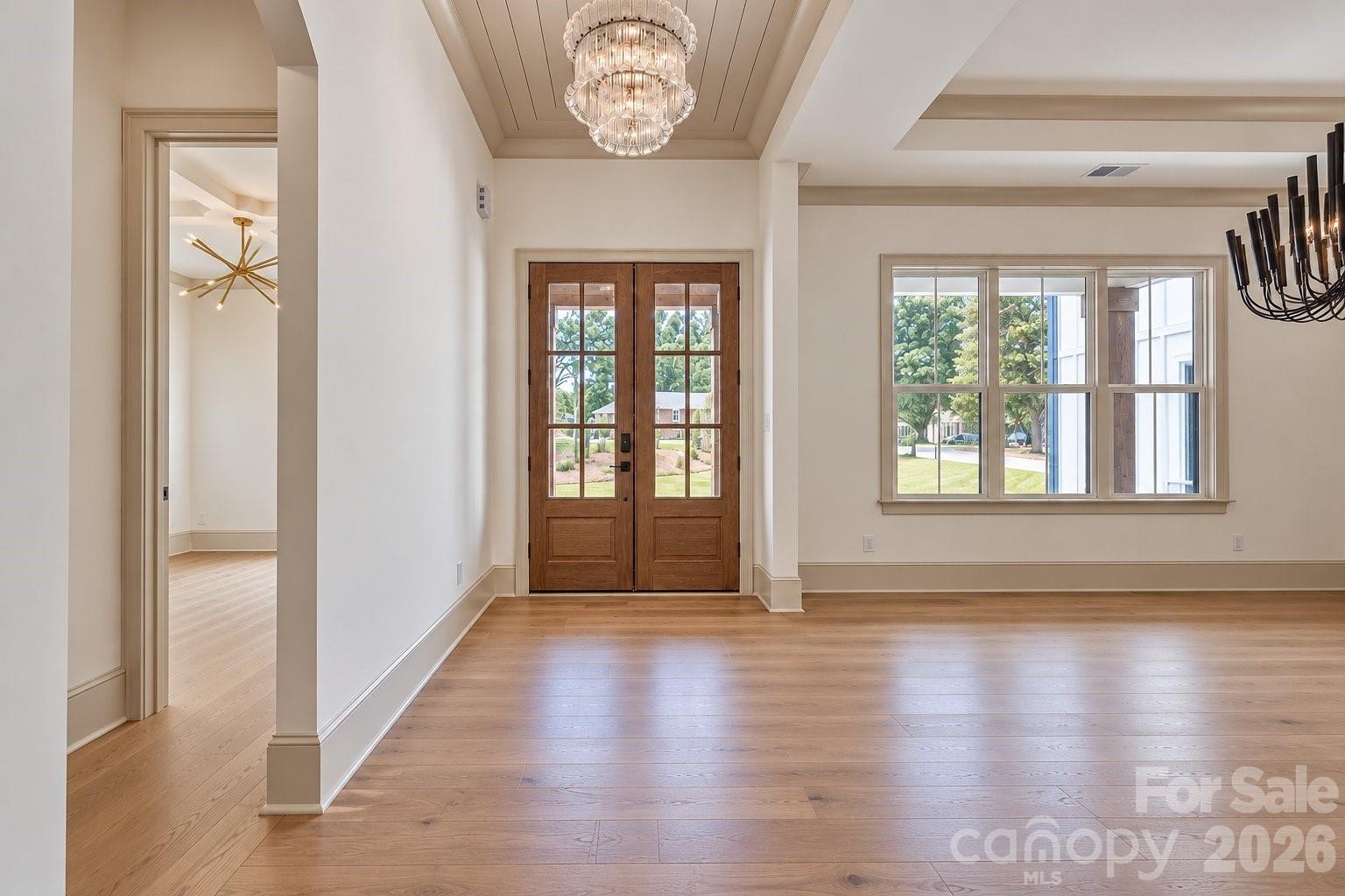Unfurnished entry hall with wood-and-glass double doors, wide-plank floors and a crystal chandelier.