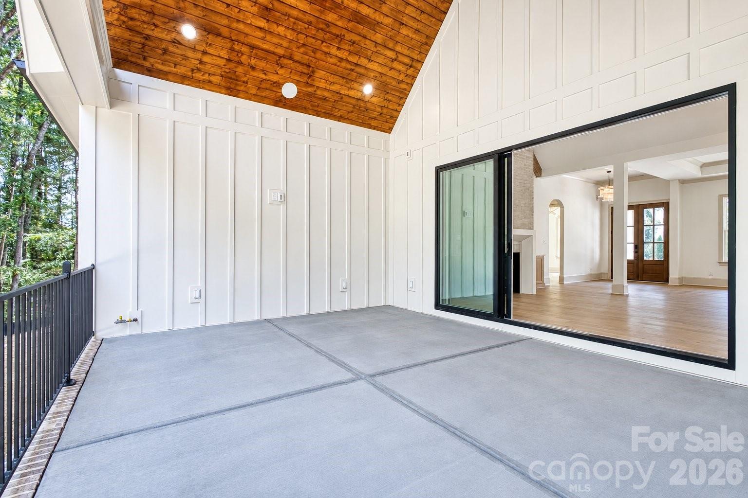 Covered patio with a high wood ceiling, concrete floor, and large sliding glass doors.