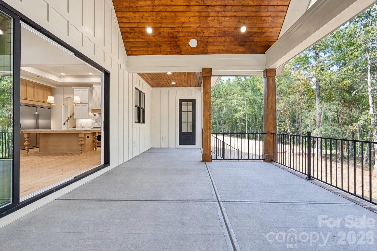Covered porch with a wood-plank ceiling and wooded views, opening onto a kitchen with a large island.