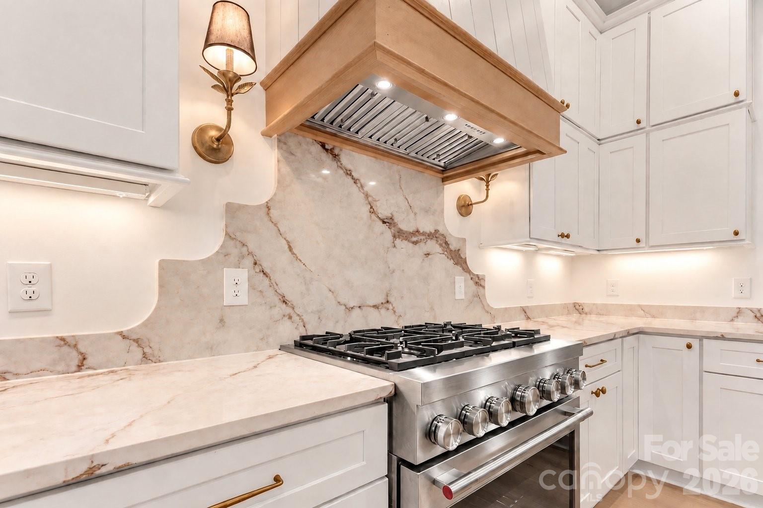 Kitchen with a stainless-steel gas range beneath a wood-trimmed hood and marble-look backsplash.