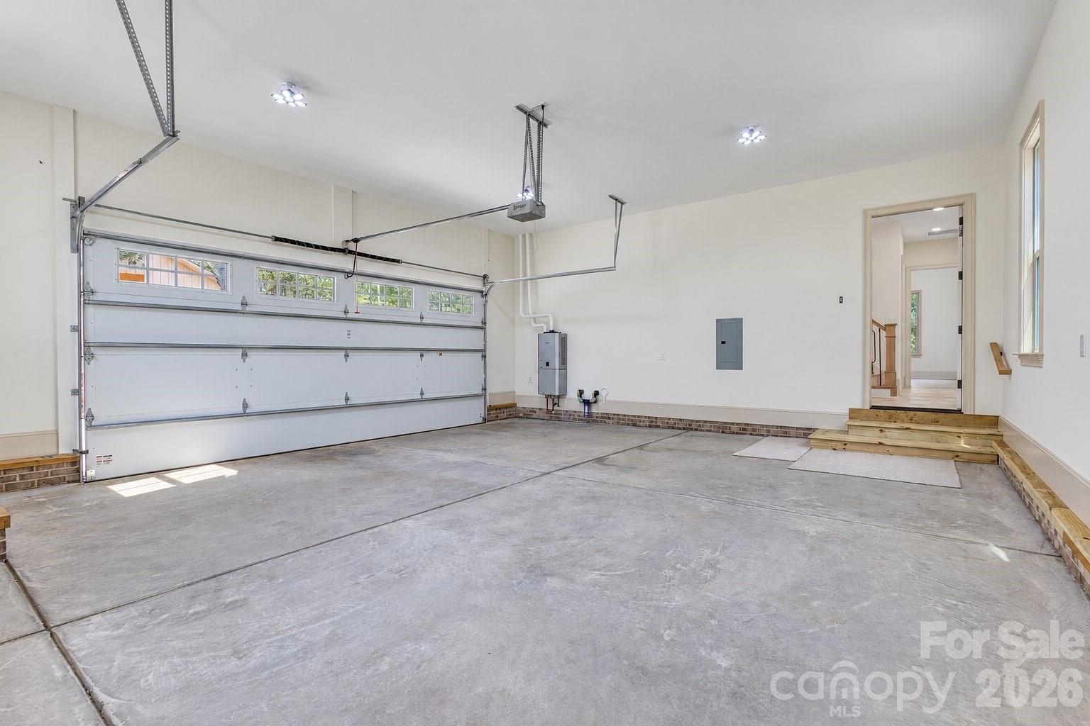 Empty garage with a broad concrete floor, high ceiling, and double garage door with windows.