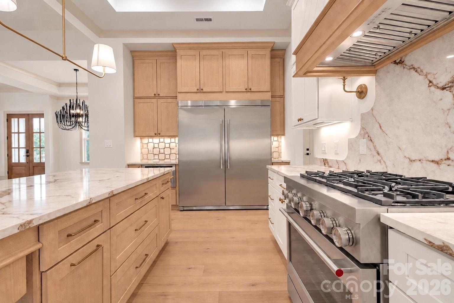 Kitchen with marble island, light wood cabinetry, stainless refrigerator, and professional gas range.
