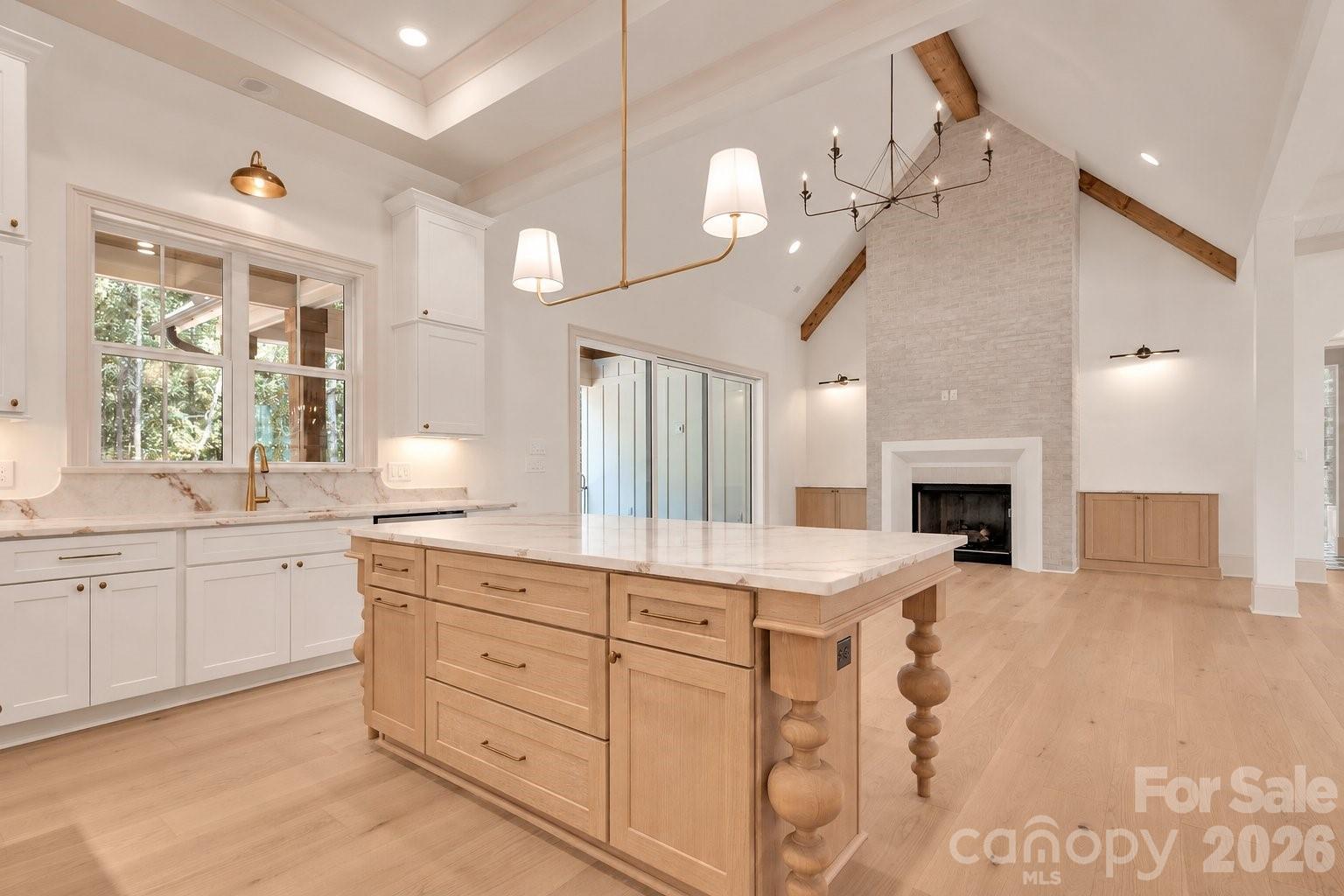 Open kitchen with a large wood island and vaulted living area centered on a tall stone fireplace.