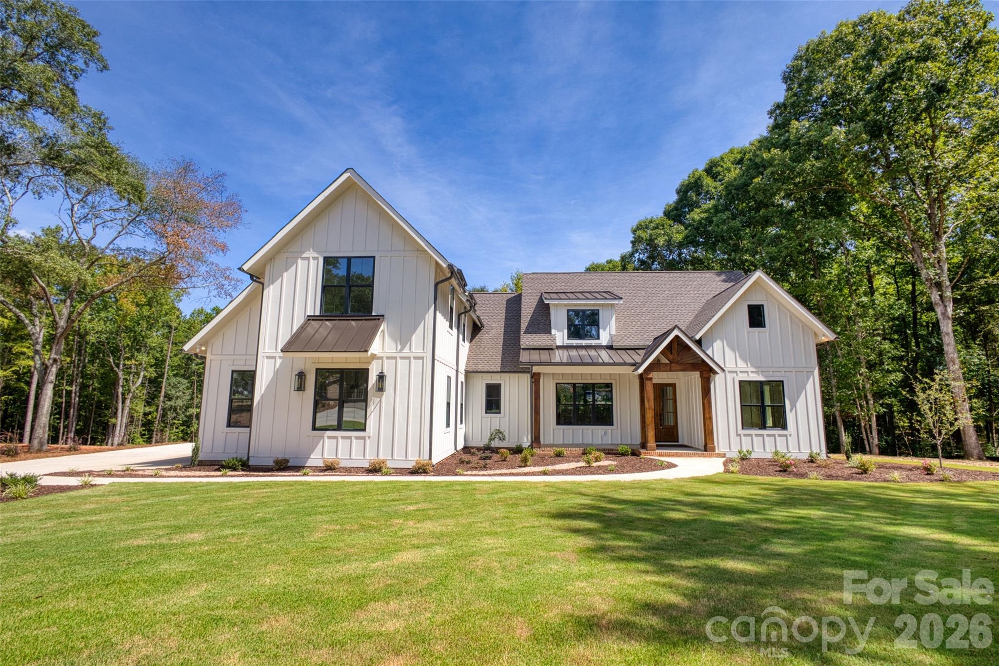 White two-story home with a wood-accented entry, broad lawn, and mature trees.
