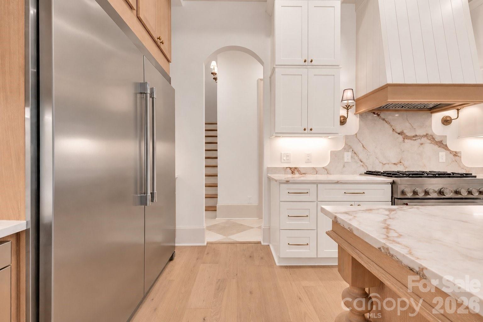 Kitchen with white cabinets, stainless appliances, marble-look surfaces, and a wood-topped island.