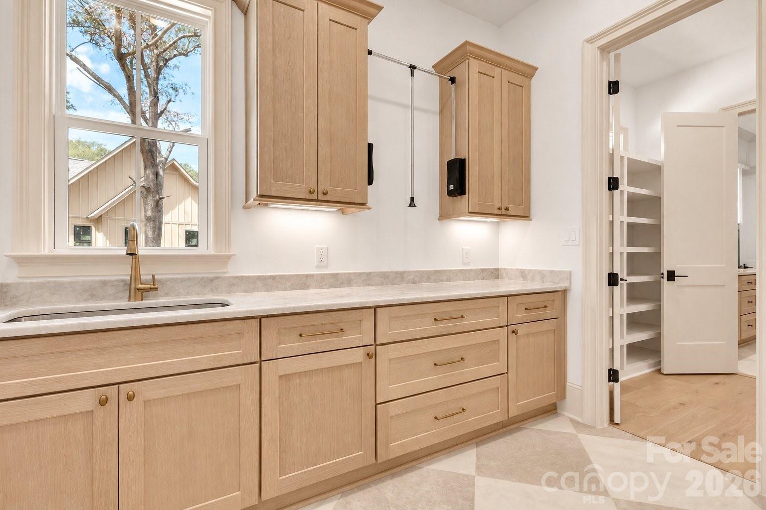 Laundry room with light wood cabinetry, a utility sink, and a hanging rod.
