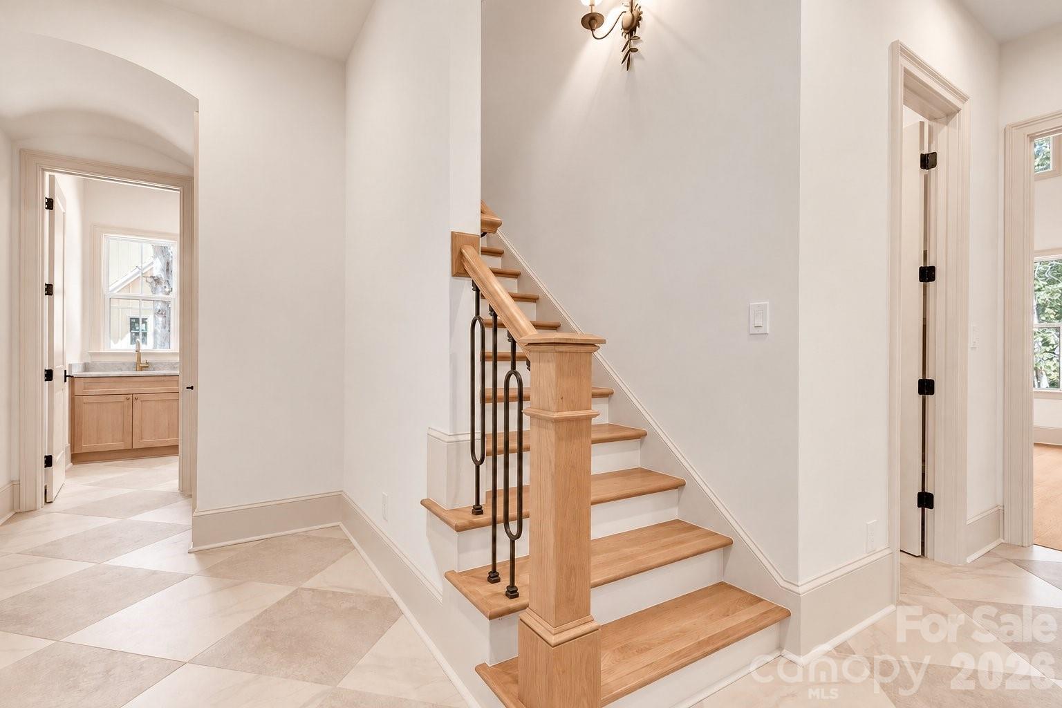 Entry foyer with a light wood staircase, dark metal balusters, and large pale tile flooring.