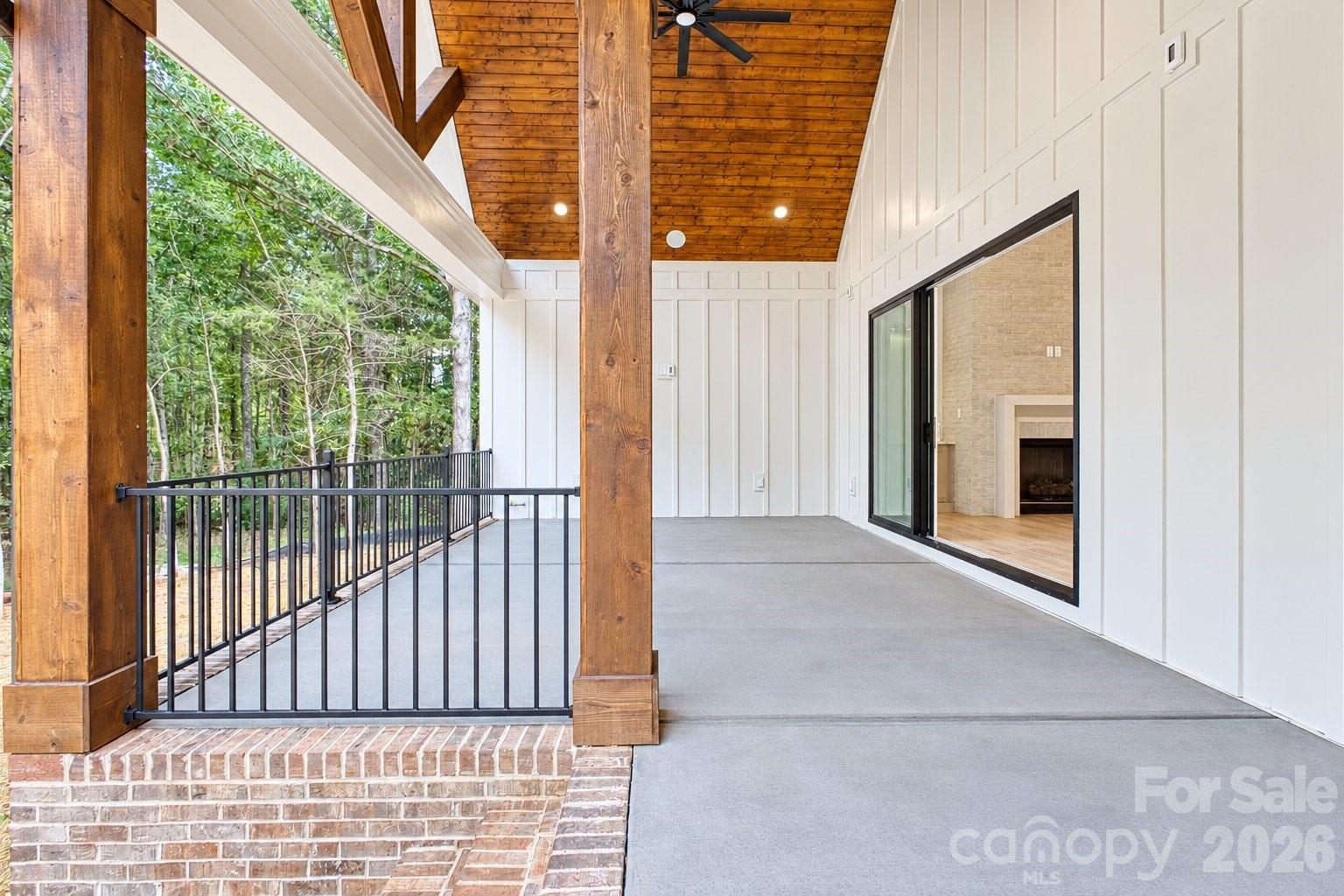 Covered porch with exposed timber beams, a black railing, and sliding doors opening toward a fireplace.