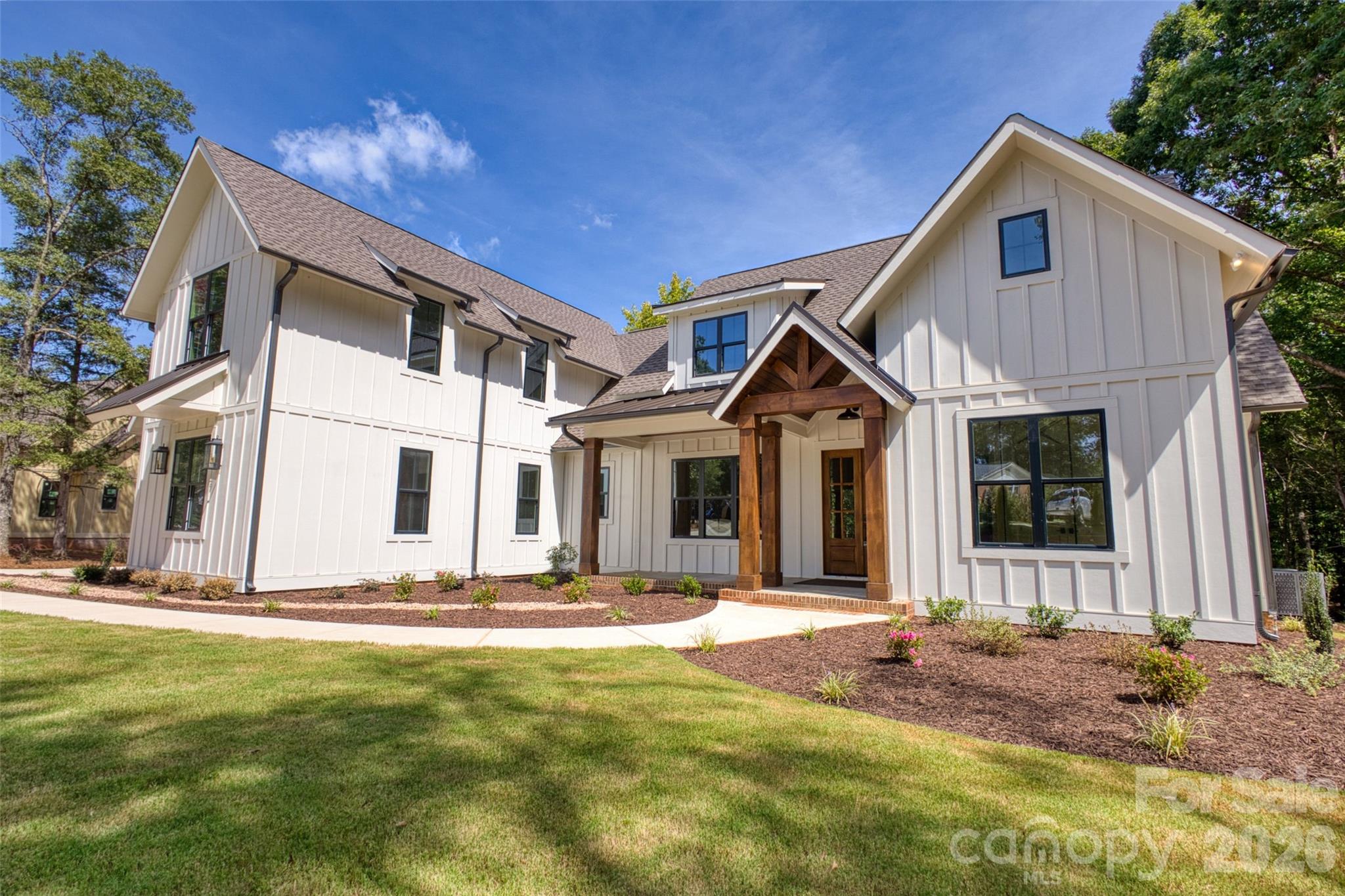 White two-story home with a timber-covered entry porch and landscaped front yard.