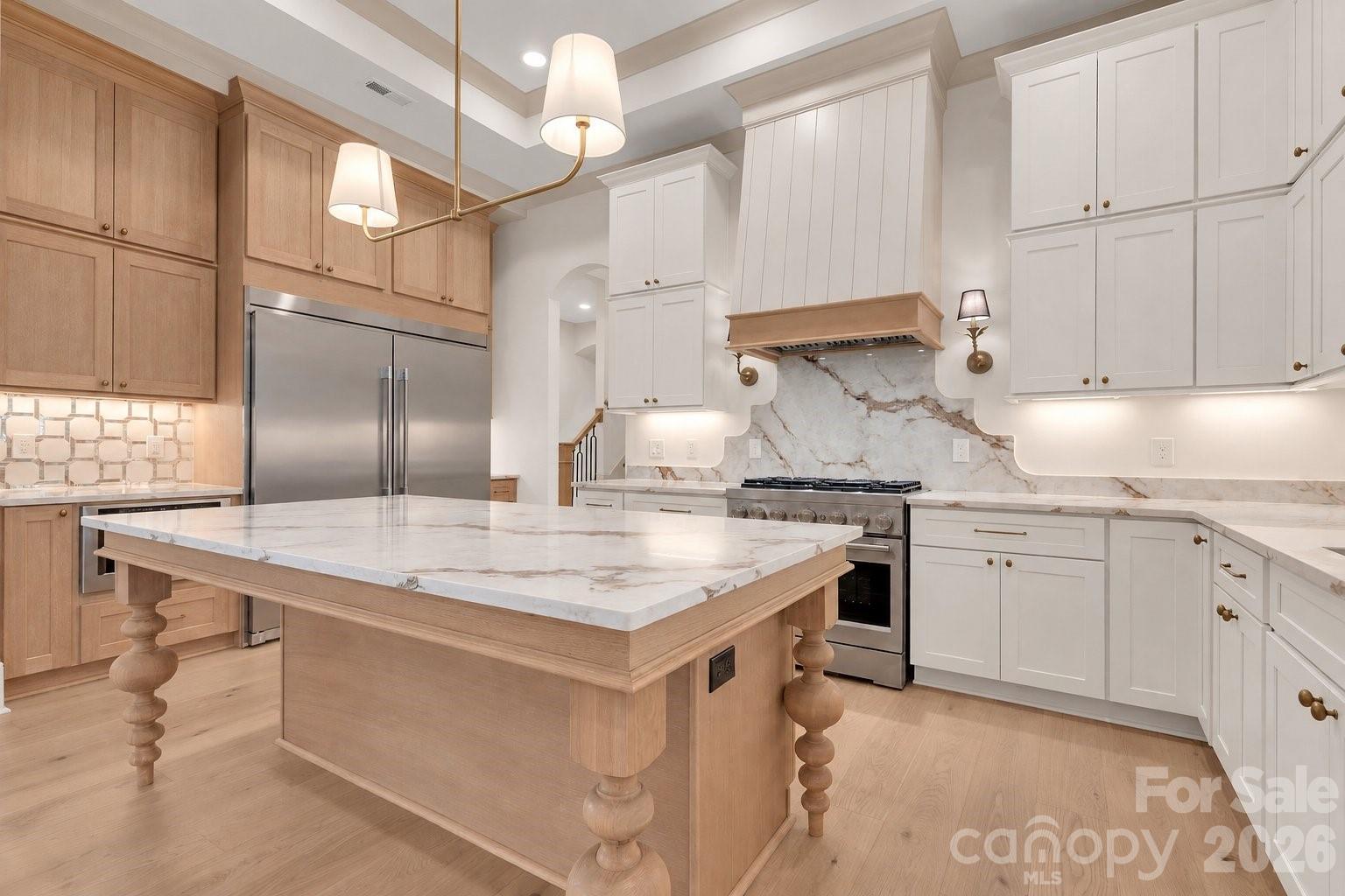 Kitchen with a large marble-topped wood island, white cabinetry, and stainless-steel appliances.
