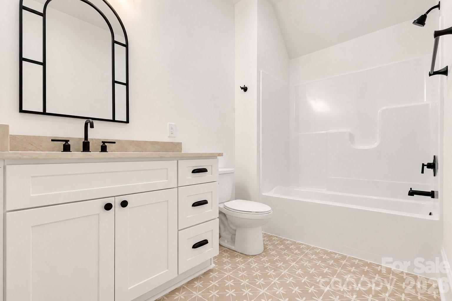 Bathroom with a white vanity, black fixtures, and patterned floor tile beside a tub-shower.