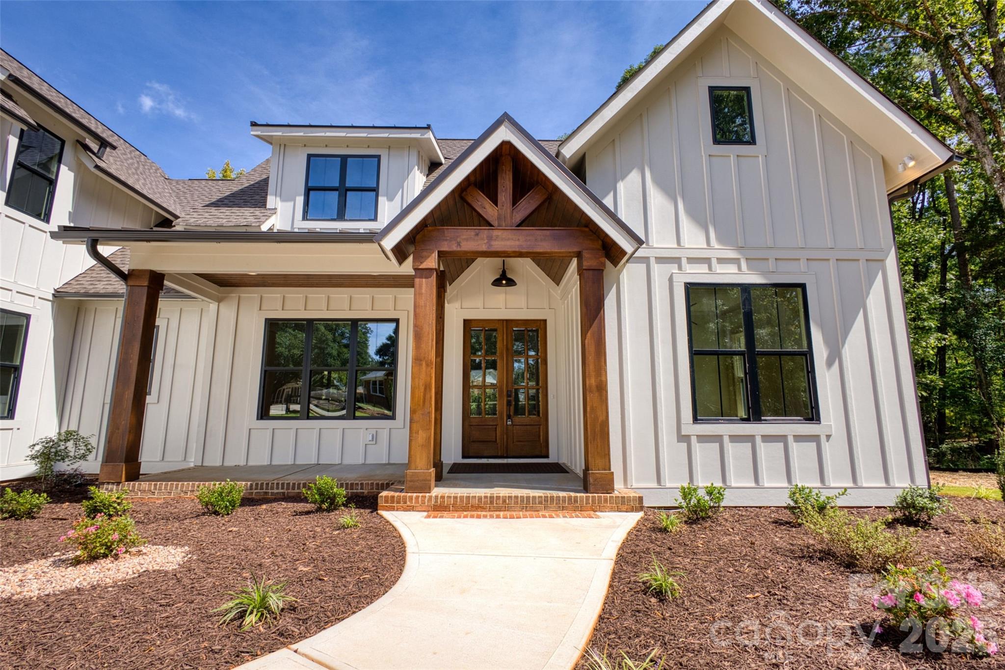 White two-story house with a timber-framed entry and curved walkway through landscaped beds.