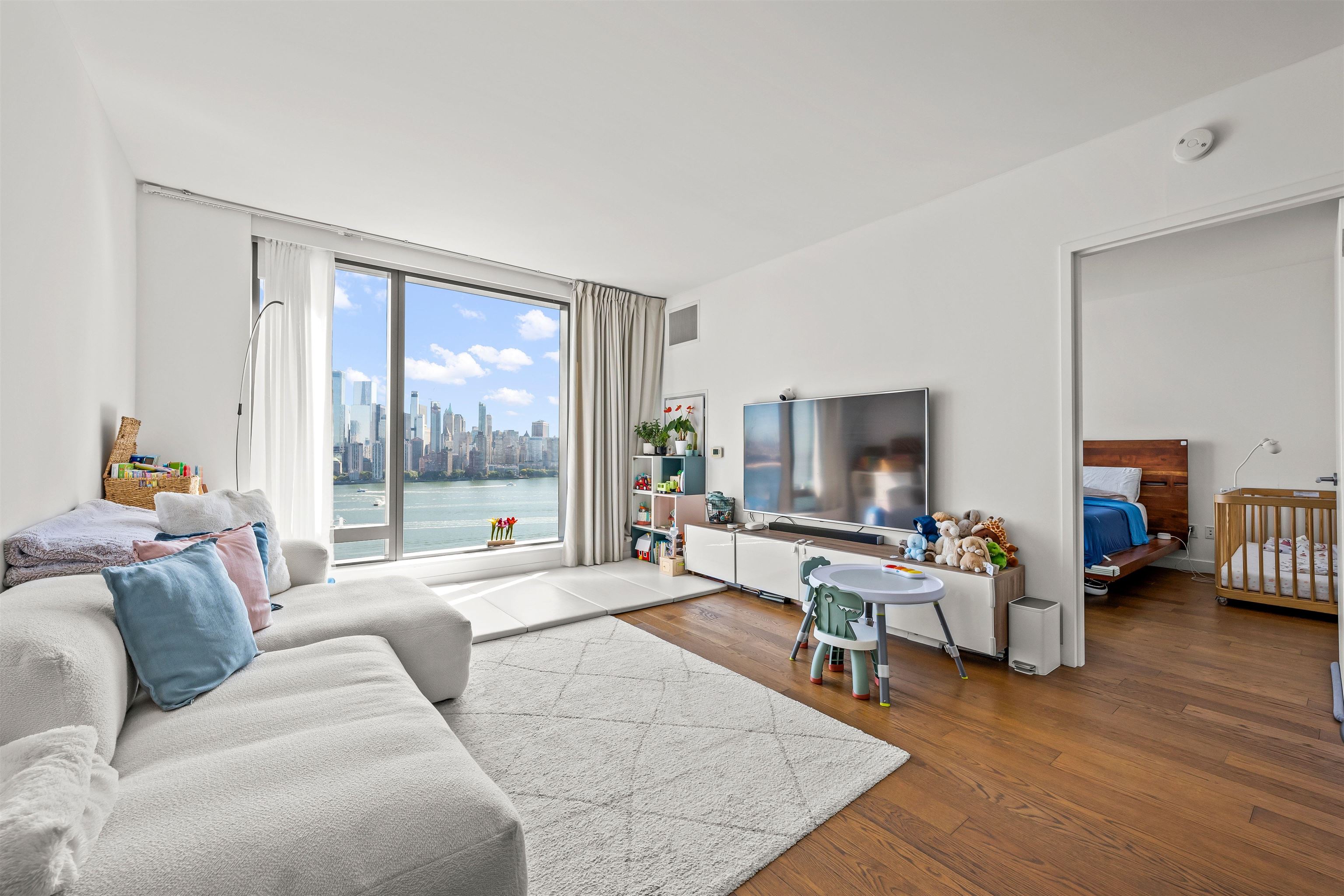 Furnished living room with a wide Hudson River and Manhattan skyline view through floor-to-ceiling windows.