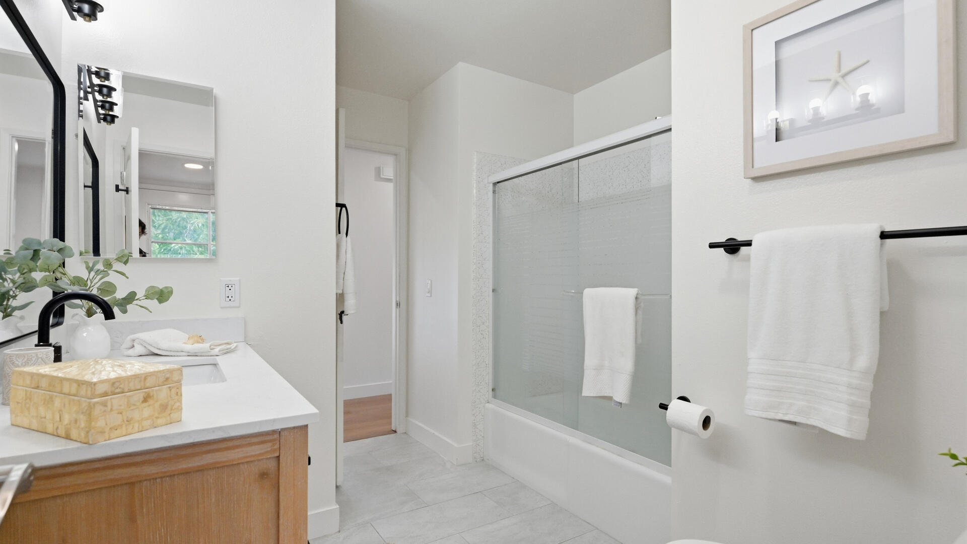 Bright bathroom with a wood vanity, large mirrors, and a glass-enclosed tub and shower.