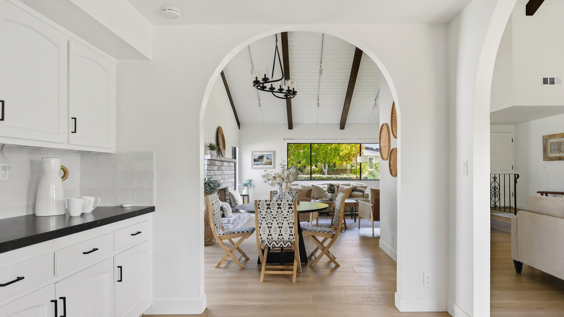 Open-plan kitchen, dining, and living area with an arched opening and vaulted beamed ceiling.